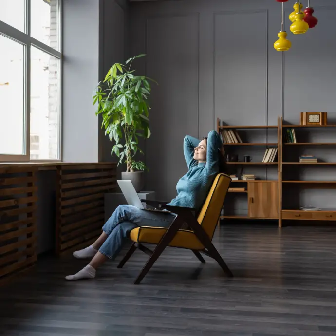 Chica joven sentada con un portátil en las piernas mirando por la ventada