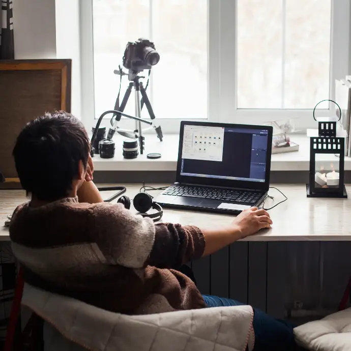 Chico joven trabajando desde su casa con un portatil y cámara de fotos
