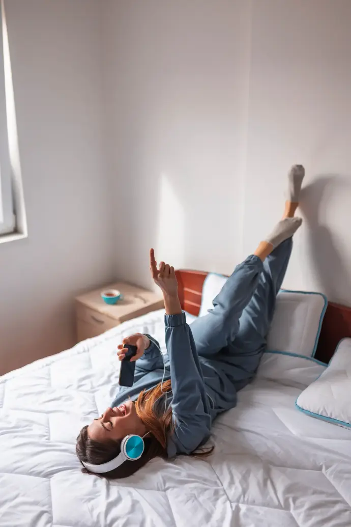 Chica joven tumbata en la cama con los pies en el cabecero cantando