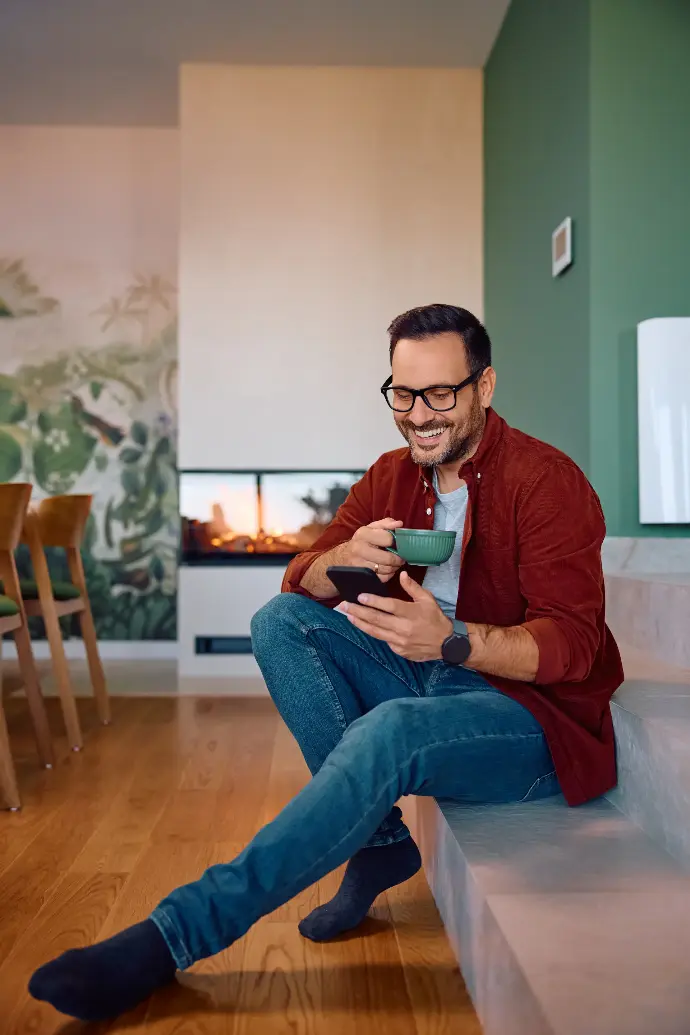 Hombre adulto disfrutando de un cafe en su sofá y viendo el móvil