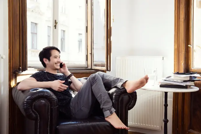 Hombre asiático sentado en un sillón en su piso hablando por teléfono