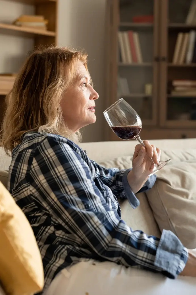 Mujer de lado sentada en el sofá bebiendo una copa de vino