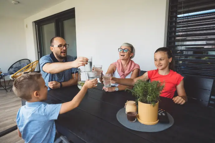 Familia sentada en una mesa con vasos de agua brindando